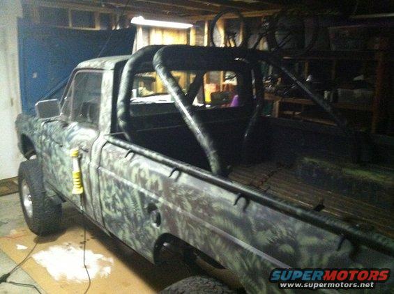 Pickup truck with camouflage paint and a roll cage inside, parked in a garage