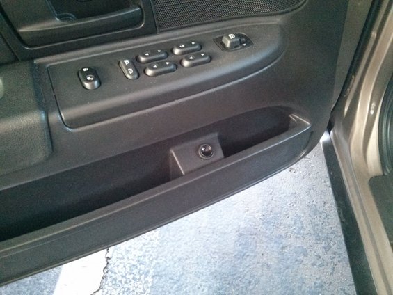 Interior door panel with window controls and a small black button in a cubby