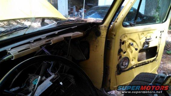 Yellow vehicle interior with door removed, showing dashboard and steering wheel. Another car is visible in the background