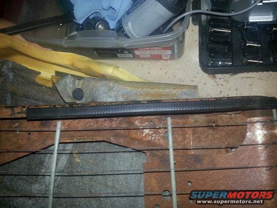 Rusty car seat frame with foam padding and a black trim piece. Tools and storage bin in background