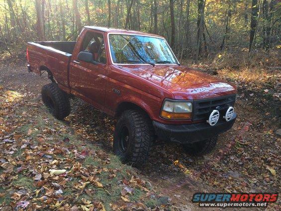 Red 1996 Ford F-150 with off-road tires on a wooded trail