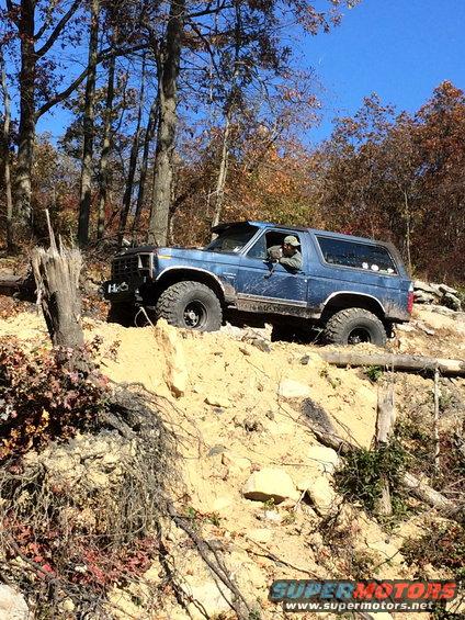 Blue SUV with large tires driving on a dirt hill in the woods