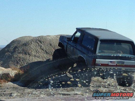 Ford Bronco climbing over rocks and dirt, rear view