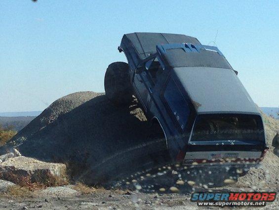 Blue SUV with large tires climbing a rocky hill, rear view