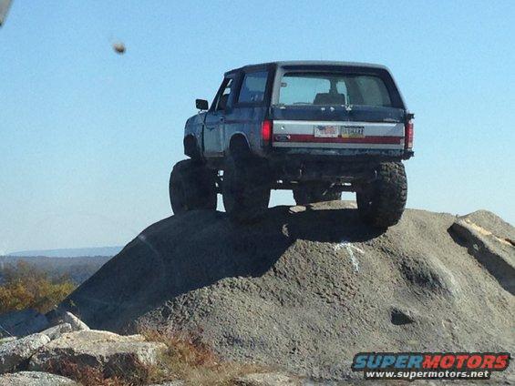 Blue SUV with large tires on a rocky incline, rear view. License plate is visible