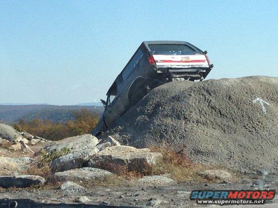 dark SUV tilted on a pile of rocks, with a red stripe on the back