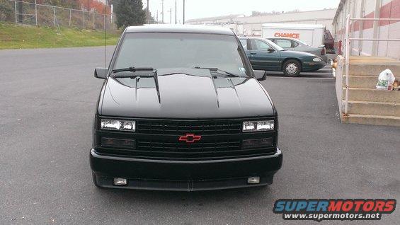 Front view of a black pickup truck with a red Chevrolet emblem on the grille. It has a hood scoop