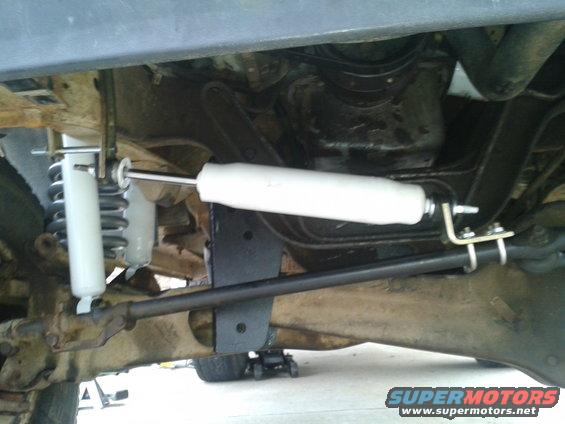 Undercarriage of a vehicle showing suspension components and steering linkage. White shock absorbers are visible