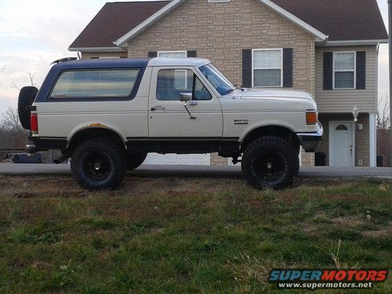 Side view of a white and blue 1988 Ford Bronco with a spare tire on the back