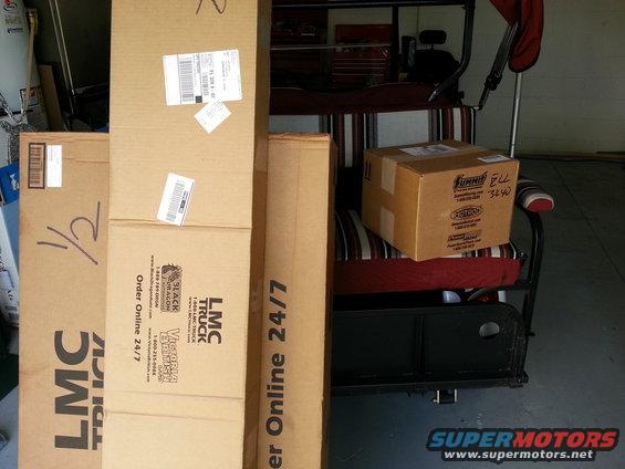 Boxes from LMC Truck and Summit Racing sit on a golf cart in a garage