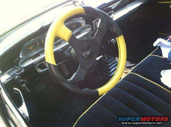 Interior shot of a car with a two-tone yellow and black steering wheel, a floor shifter, and black seats with yellow piping