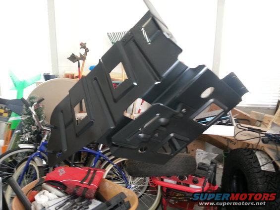 Black metal undercarriage shield with cutouts, angled upwards, in a cluttered garage with bicycles