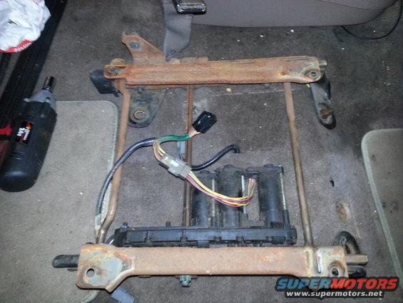 Rusted metal seat frame with black electrical components and colorful wires, on carpeted floor