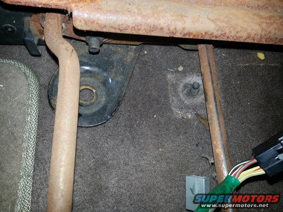 Close-up of rusty seat mounting hardware and wiring harness in a vehicle interior