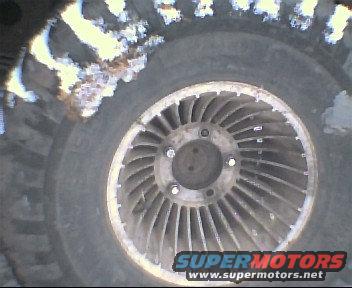 Aluminum alloy wheel with 15 spokes and a worn tire, partially covered in snow and dirt