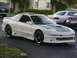 1994 Ford Probe - A white Ford Probe with a grey hood and black rims is parked on asphalt with other vehicles in the background.