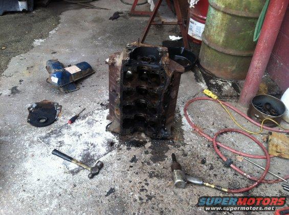Engine block, valve covers, oil pan, hammer, screwdriver, and air tool on concrete floor