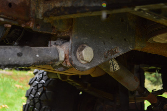 Undercarriage view of a vehicle showing suspension components and a tire. Text on a shock absorber is partially visible