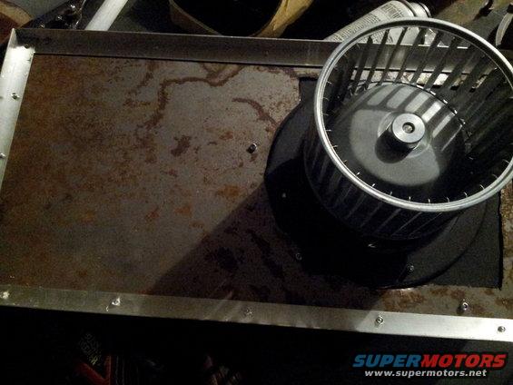 Blower motor assembly on a rusty metal panel with visible water stains