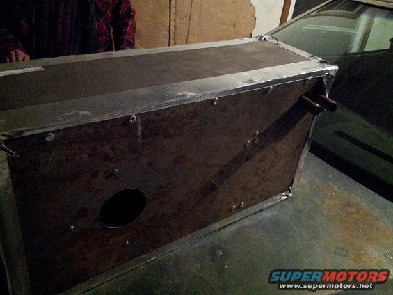 Custom metal box with rivets and a circular cutout sits on the hood of a car