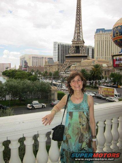Woman posing on a balcony with the Eiffel Tower replica and Las Vegas Strip hotels in the background