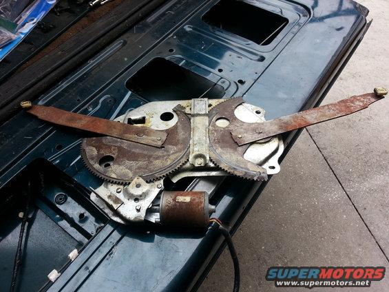 Rusty window regulator mechanism with motor on dark green metal surface