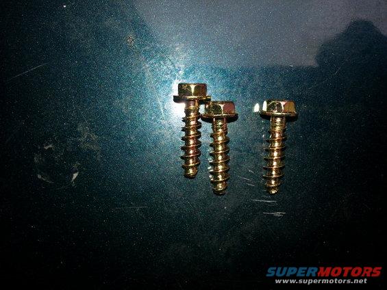 Three gold screws on a dark green, scratched surface. A watermark reads SUPERMOTORS