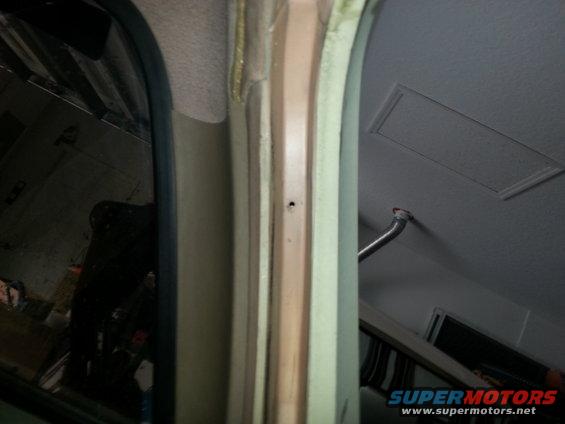 Close-up of a car's interior door frame and ceiling panel. A small hole is visible in the frame