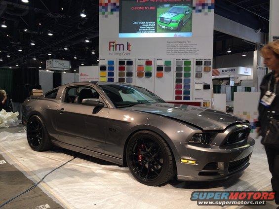 Gray Ford Mustang with black wheels and red brake calipers, hood open, at a car show