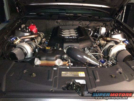 Twin-turbocharged V8 engine with custom intake and intercooler piping. Engine cover reads '5.0 Coyote'
