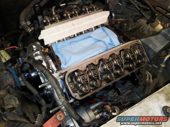Engine block with valve covers removed, showing rocker arms and springs. Blue cloth covers part of the intake