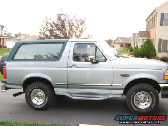 Side view of a silver 1996 Ford Bronco with a green top, parked in a driveway