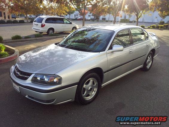 Silver Chevrolet sedan parked on asphalt, white minivan in background