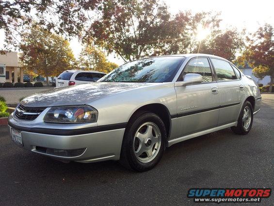Silver 2001 Chevrolet Impala parked outside with trees and a white van in the background