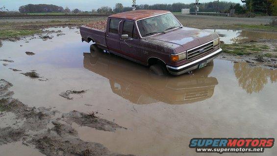 Maroon Ford F-Series truck stuck in mud, front 3/4 view, showing rust and water damage