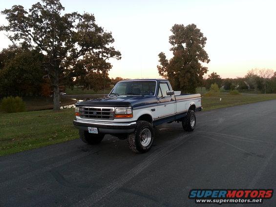 Two-tone blue and white Ford F-250 pickup truck with lifted suspension and chrome wheels parked on asphalt