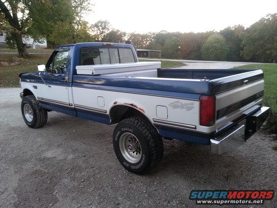 Two-tone blue and white Ford F-250 pickup truck with a toolbox in the bed, seen from the rear quarter