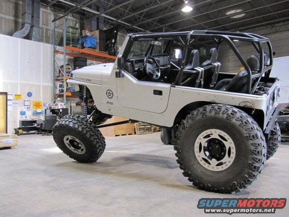 White Jeep Wrangler with roll cage and large off-road tires. Rubicon badge visible