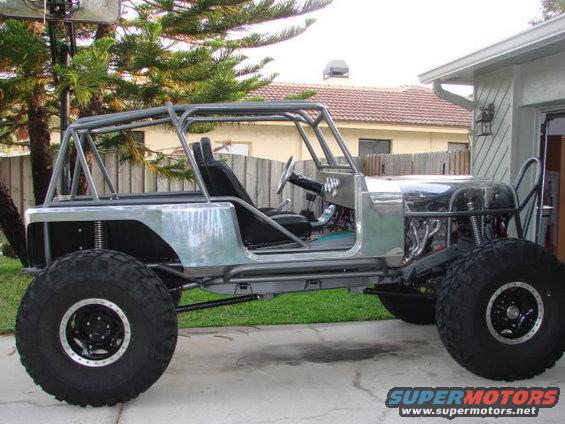 Bare metal off-road vehicle with roll cage, large tires, and exposed engine, viewed from the side