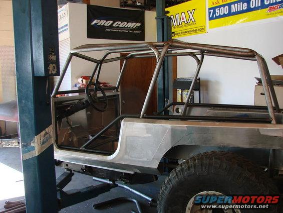 Bare metal Jeep CJ-series body with custom roll cage, viewed from 3/4 front