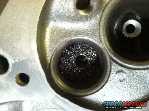 Close-up of an engine cylinder head showing two valve seats, one filled with debris