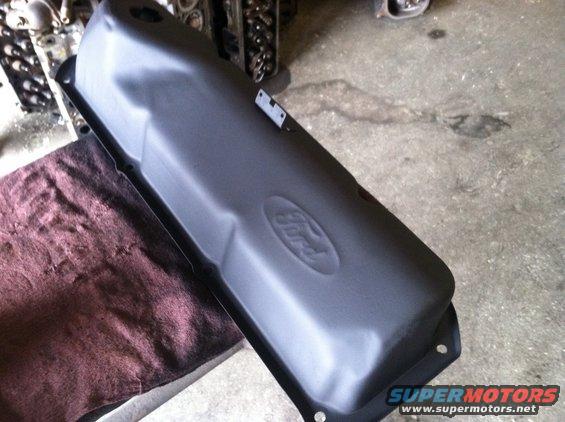 Black Ford valve cover with embossed logo, resting on a maroon cloth