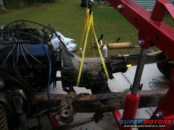 Engine and transmission assembly suspended by yellow straps from an engine hoist
