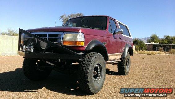Maroon 1996 Ford Bronco with a large black aftermarket bumper and winch, parked on a dirt lot