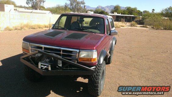 Red Ford Bronco with aftermarket bumper and winch, hood scoops, and fender flares