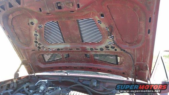 underside of red car hood with vents, showing engine parts below