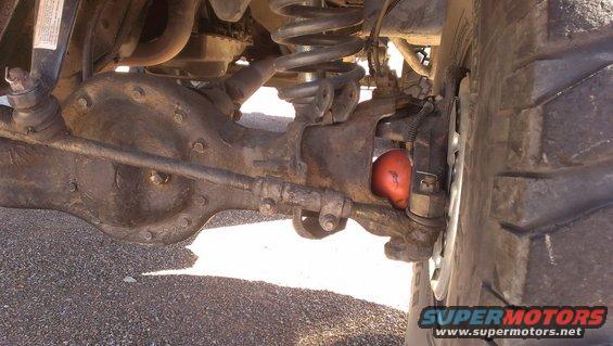 Close-up of a vehicle's front axle, differential, and suspension components. A bright orange shock absorber is visible