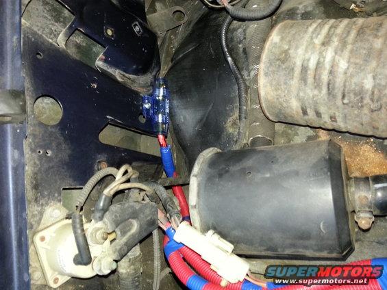 Close-up of vehicle wiring, a blue fuse box, and some engine components