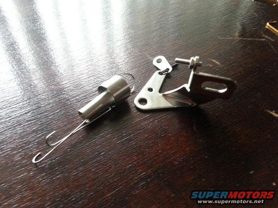 Two chrome-plated metal carburetor linkage parts on a wooden surface