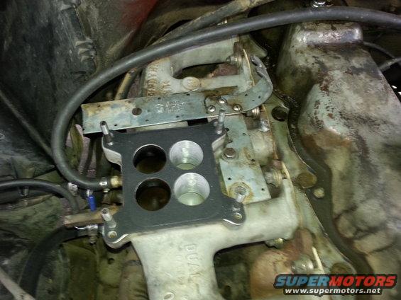 Close-up of a carburetor base plate and intake manifold with hoses attached